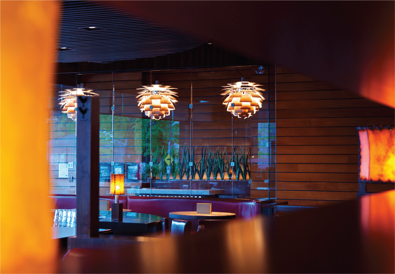 Modern interior of Cactus Club Cafe in Abbotsford featuring contemporary pendant lights with layered orange shades, floor-to-ceiling windows with wooden frames, and ambient warm lighting