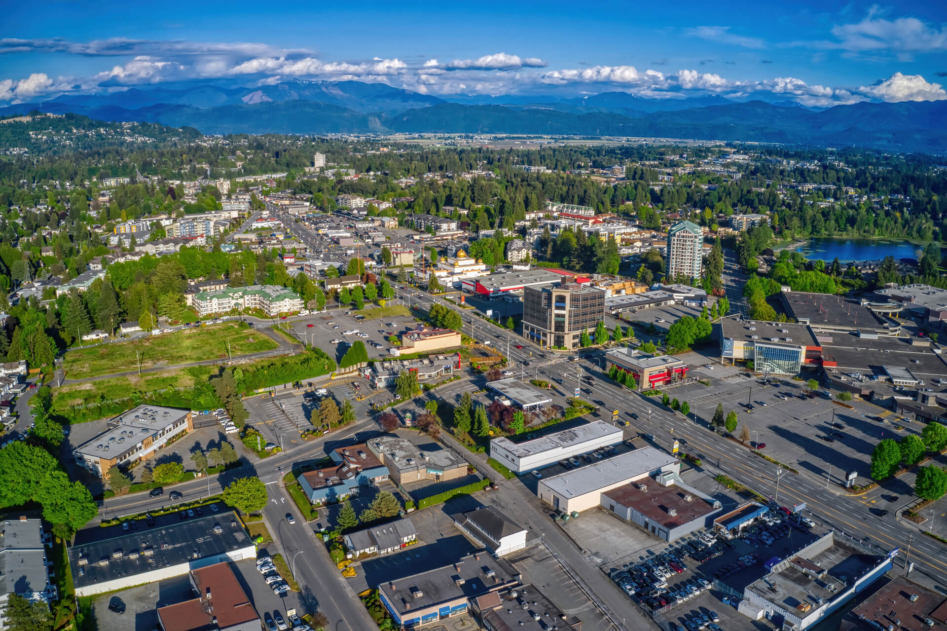 Aerial view of Abbotsford, British Columbia showing downtown commercial area with mountains and forest in the background under clear blue sky
