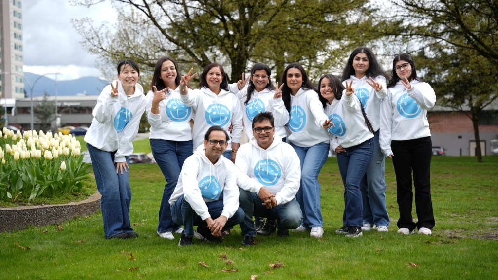 Team of dental professionals wearing white hoodies with blue smiley face logos posing together outdoors in Abbotsford
