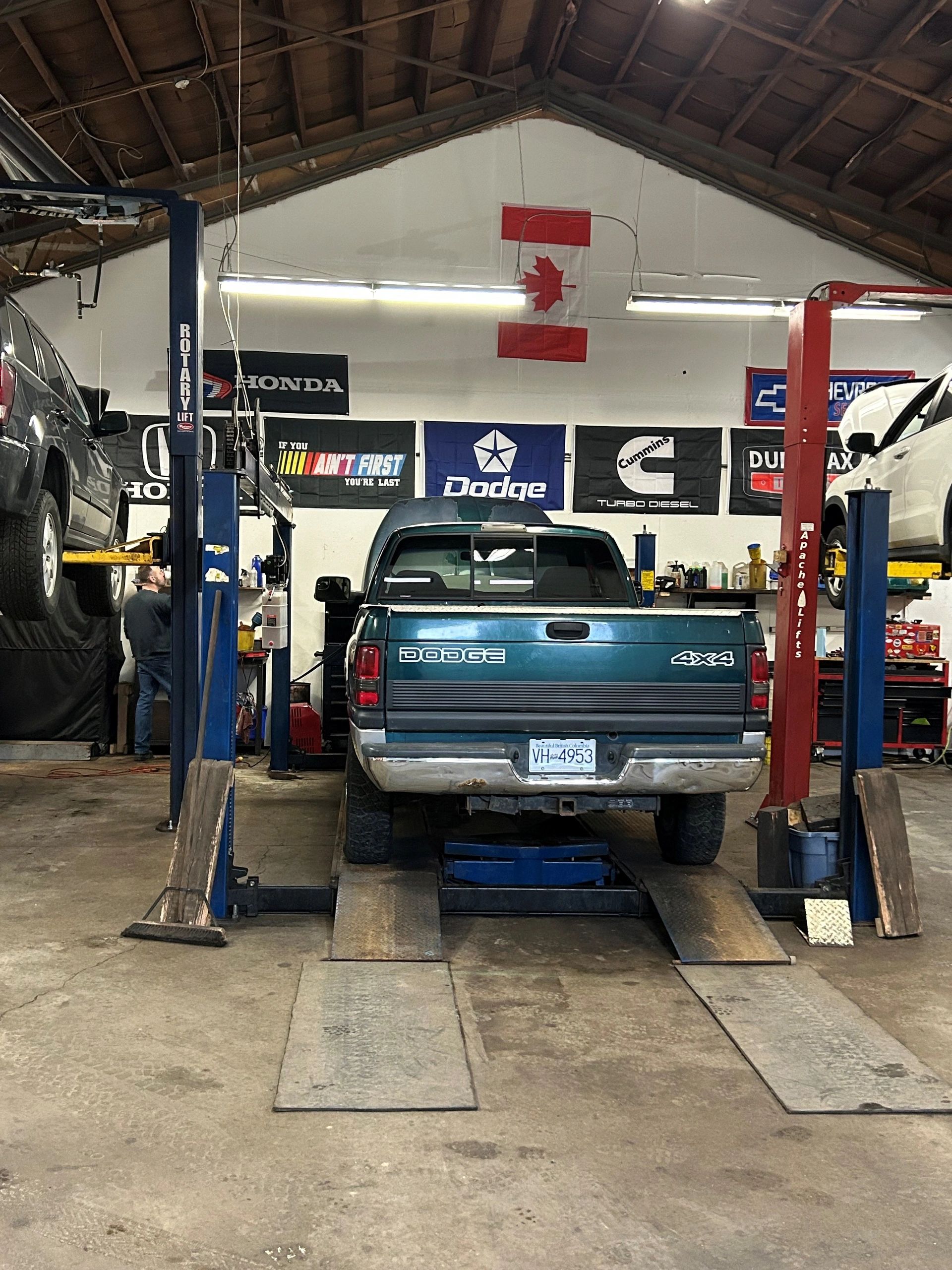 Turquoise Dodge pickup truck with 4x4 badging elevated on a red and blue hydraulic lift in an automotive service bay, with Canadian flag and brand signage visible in the background at Paul Carter Auto in Abbotsford