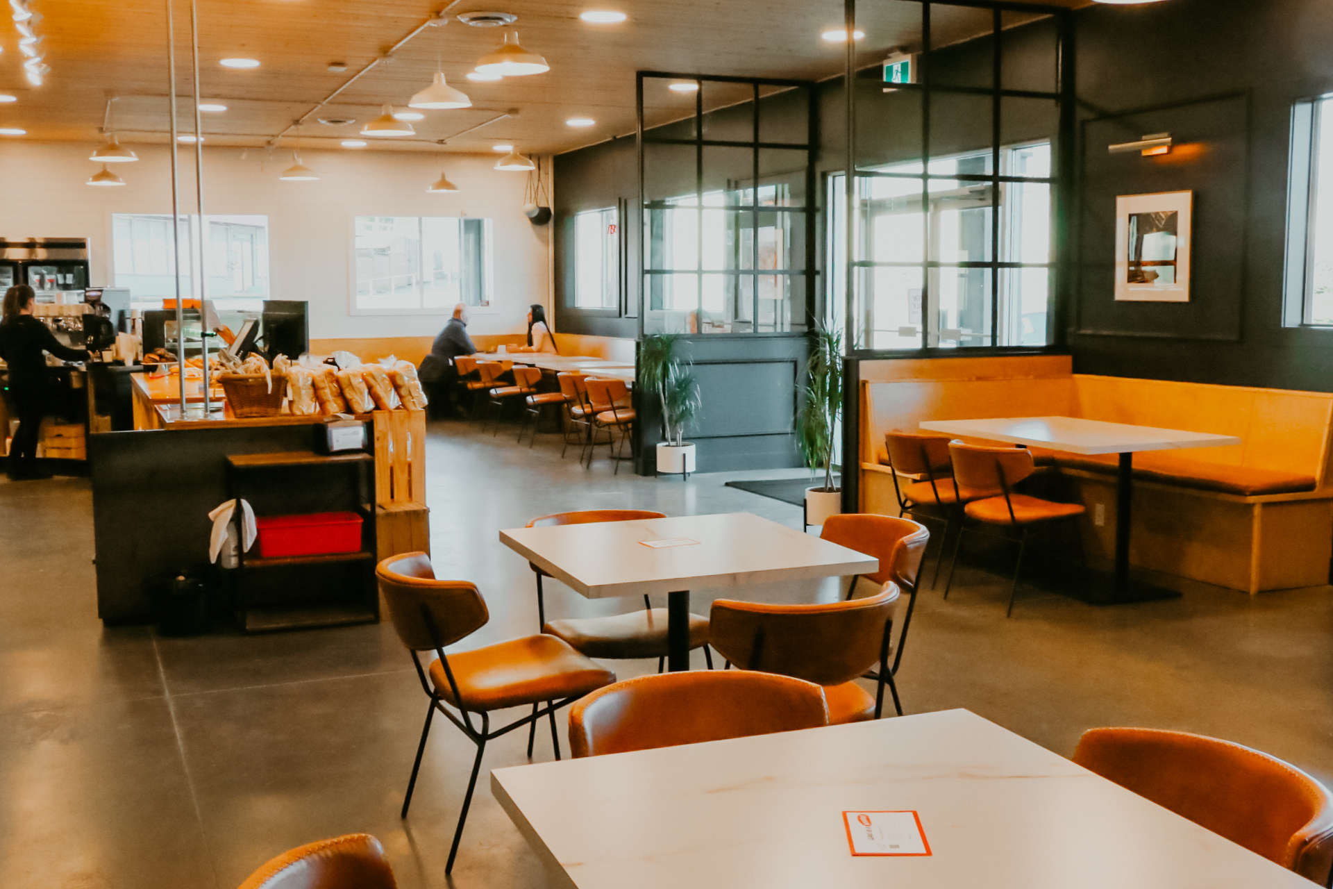 Modern cafe interior with orange and black seating, white tables, and floor-to-ceiling windows in Abbotsford