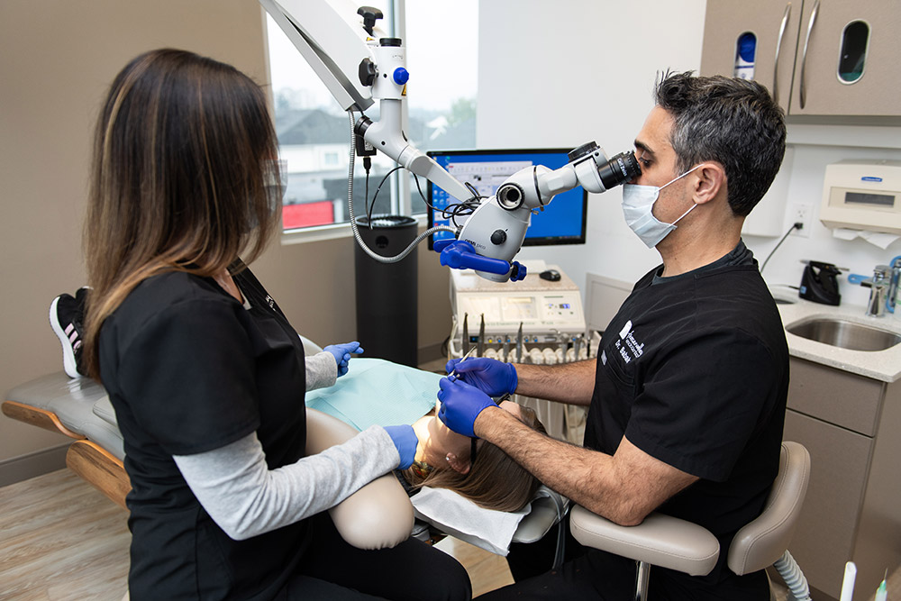 Dr. Babak Nurbakhsh performing an endodontic procedure on a patient using a surgical microscope in a modern dental office in Abbotsford