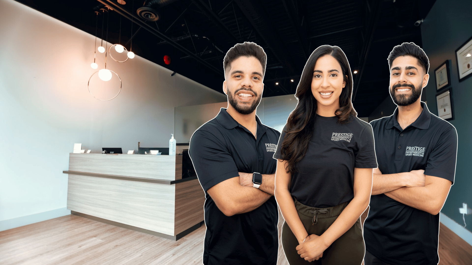 Three smiling team members wearing black Prestige branded polo shirts standing in a modern physiotherapy clinic in Abbotsford with wooden flooring and contemporary reception desk behind them