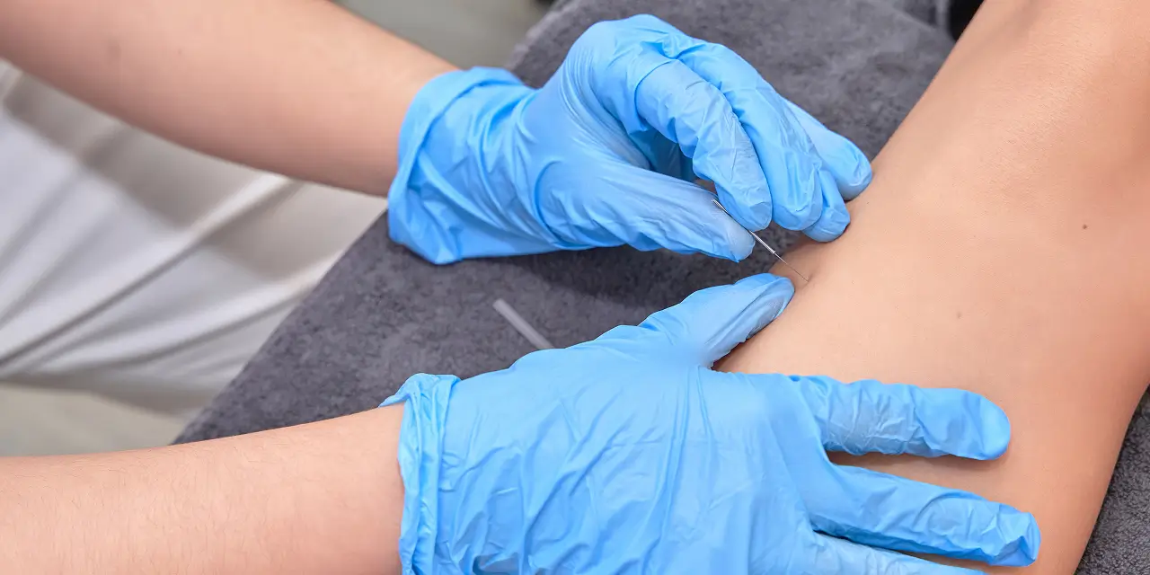Healthcare professional wearing blue nitrile gloves examining a patient's arm during a physiotherapy assessment in Abbotsford