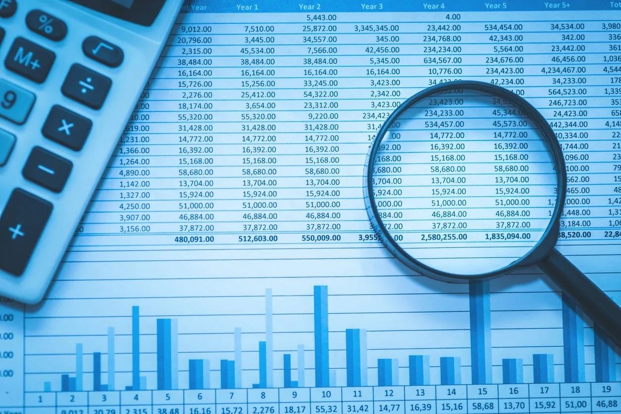 Financial data analysis with calculator and magnifying glass examining spreadsheet containing multi-year projections and bar chart for Abbotsford business records