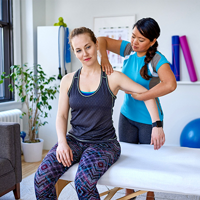 Female physiotherapist performing a shoulder assessment on a patient in a modern Abbotsford clinic setting with exercise equipment visible in the background