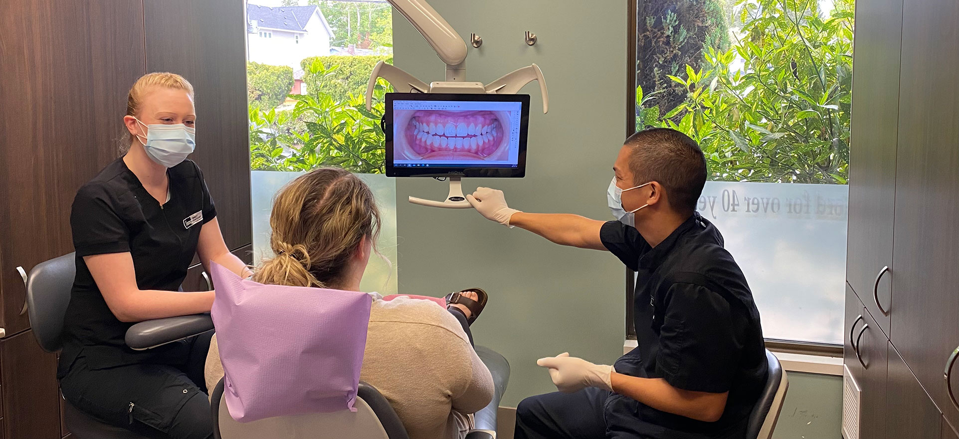 Dental consultation at Tsang Family Dentistry in Abbotsford showing patient and two dental professionals reviewing teeth imaging on a monitor