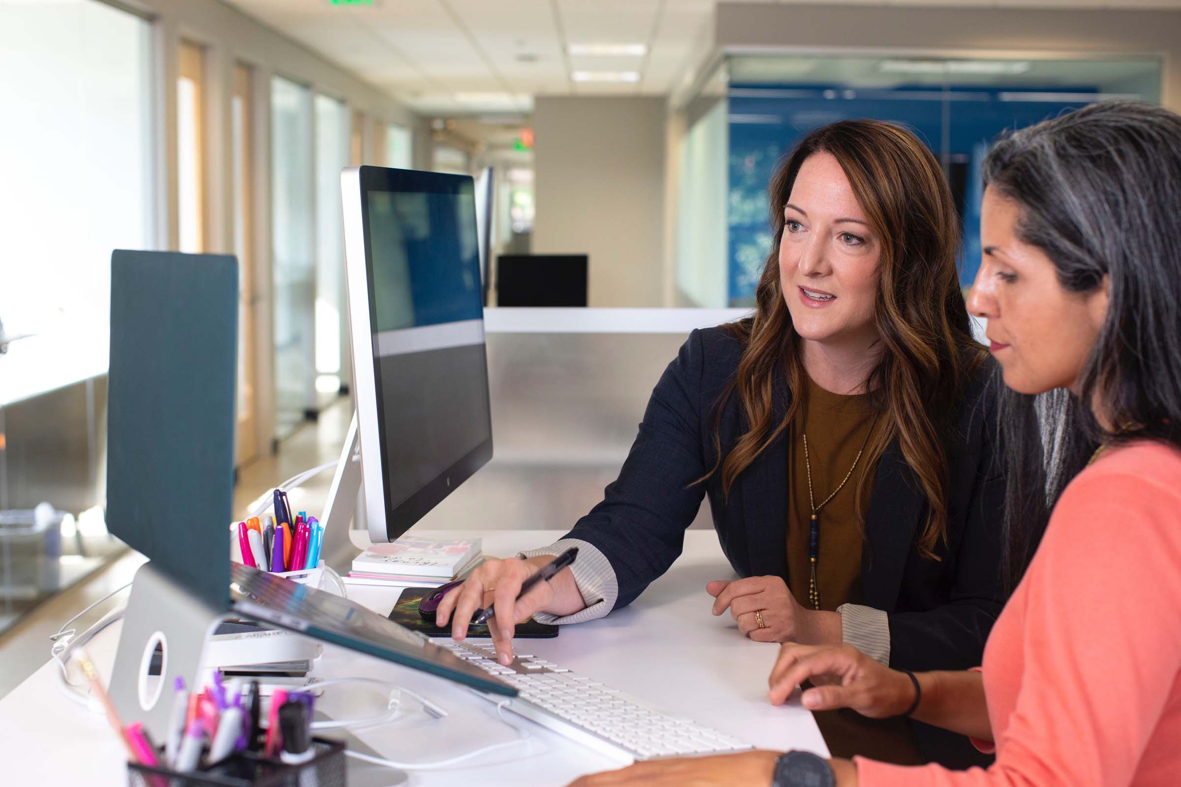 Two female professionals collaborating at a desk in a modern Abbotsford office, reviewing documents on a computer