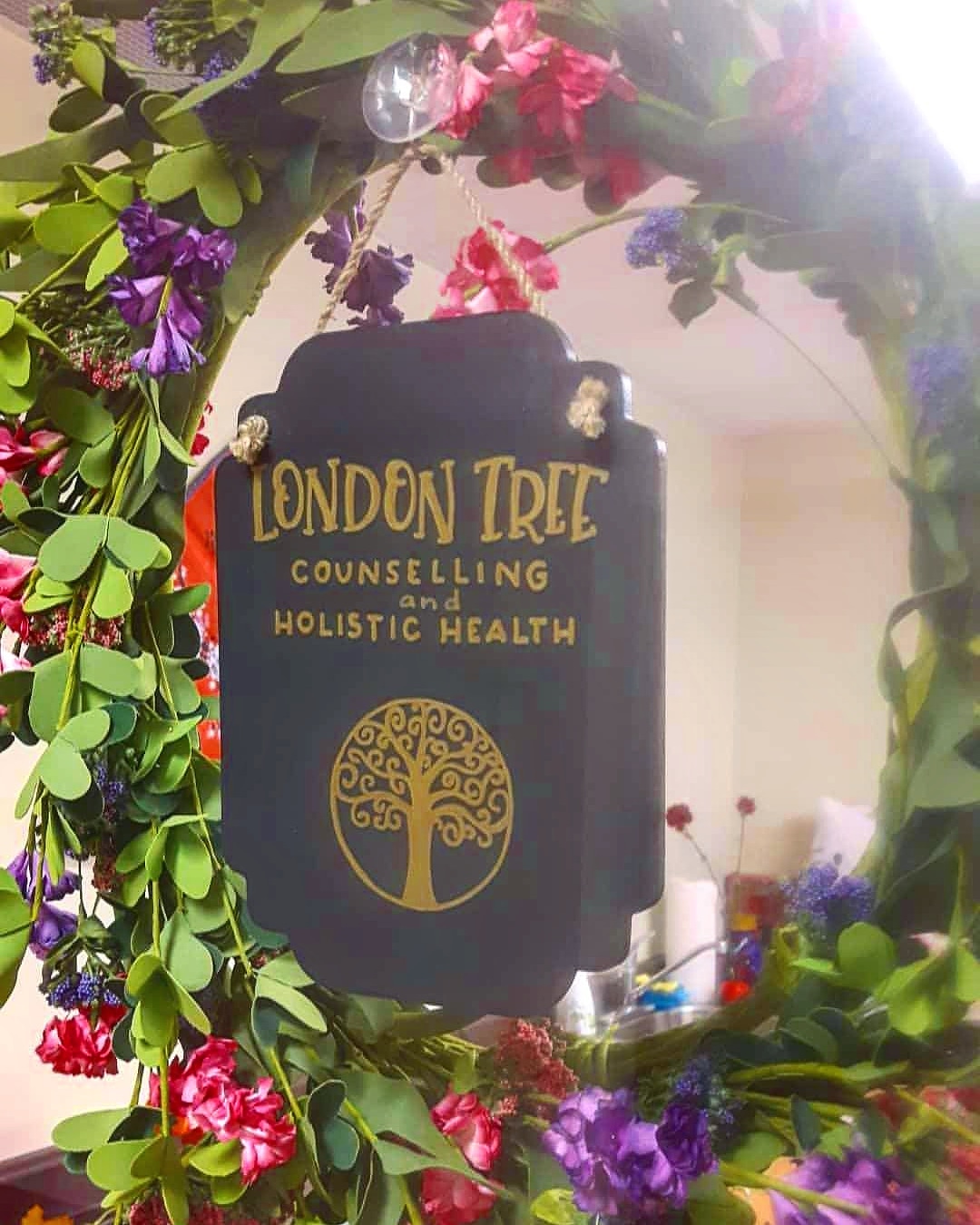 "alt_text": "A black plaque with gold lettering for London Tree Counselling and Holistic Health, featuring a stylized tree lo