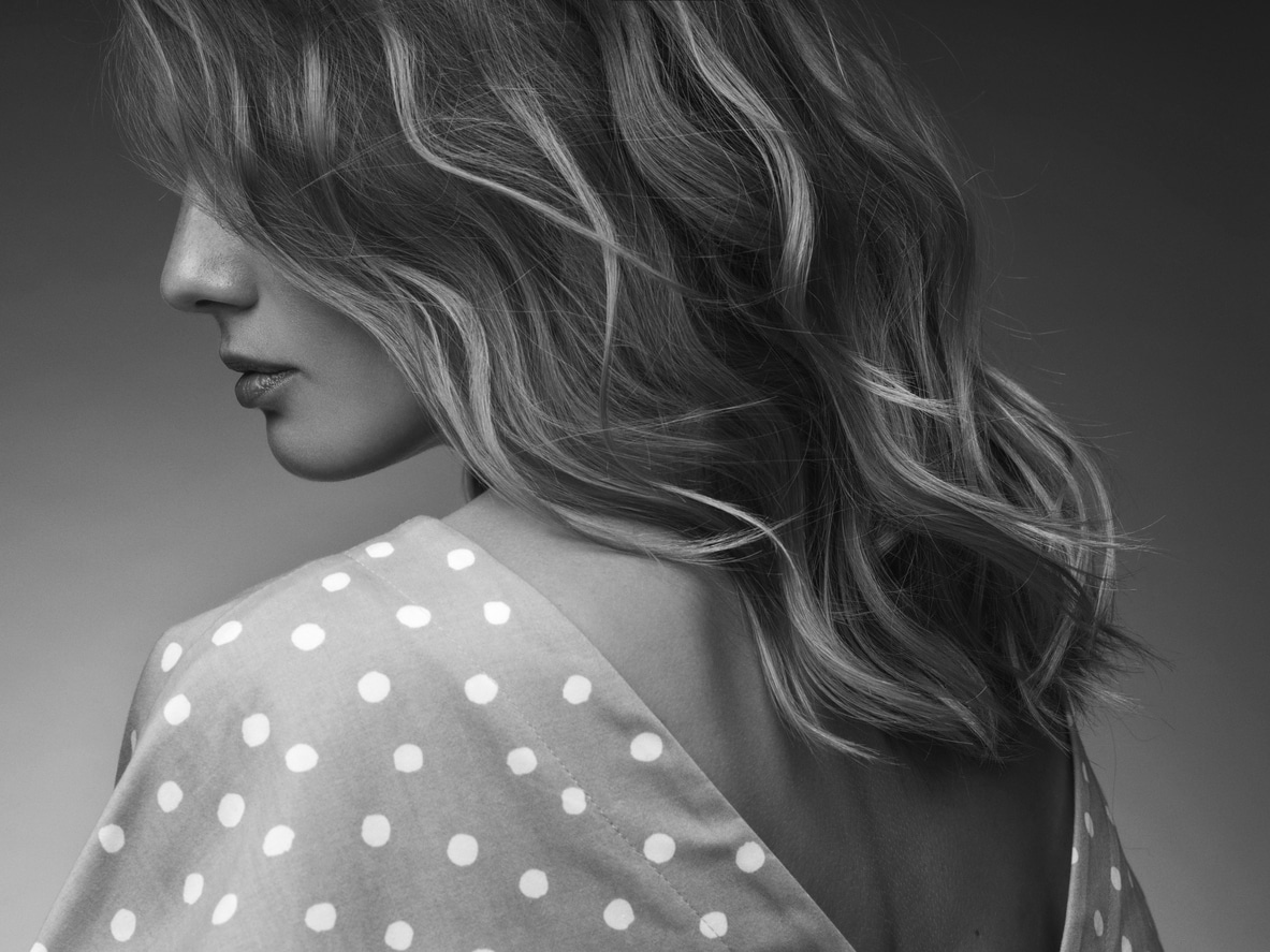 Woman with long wavy highlighted hair in profile wearing a polka dot garment at Sin 7 Salon in Abbotsford