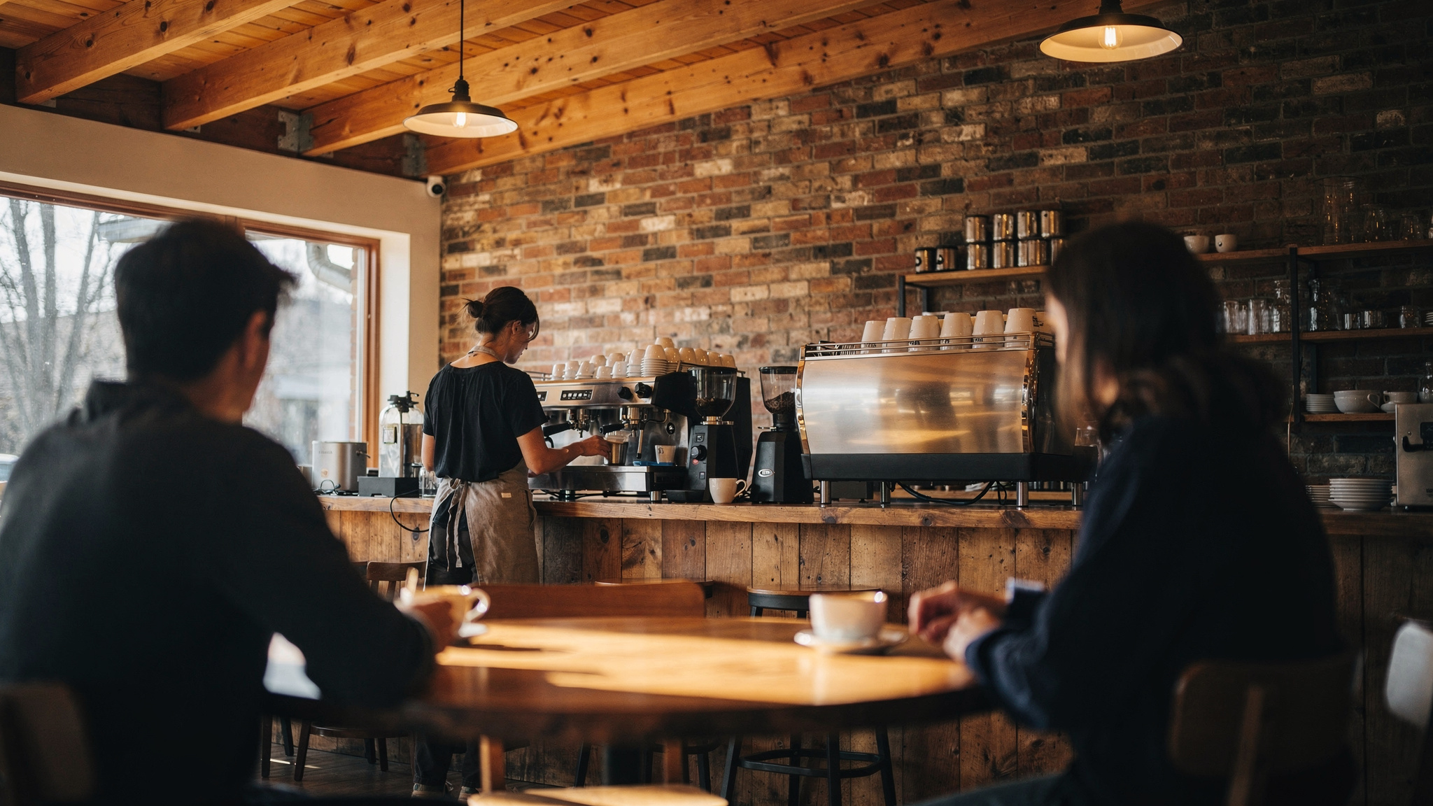 Barista preparing coffee at the espresso bar in a warm independent Abbotsford BC coffee shop, customers seated in the foreground