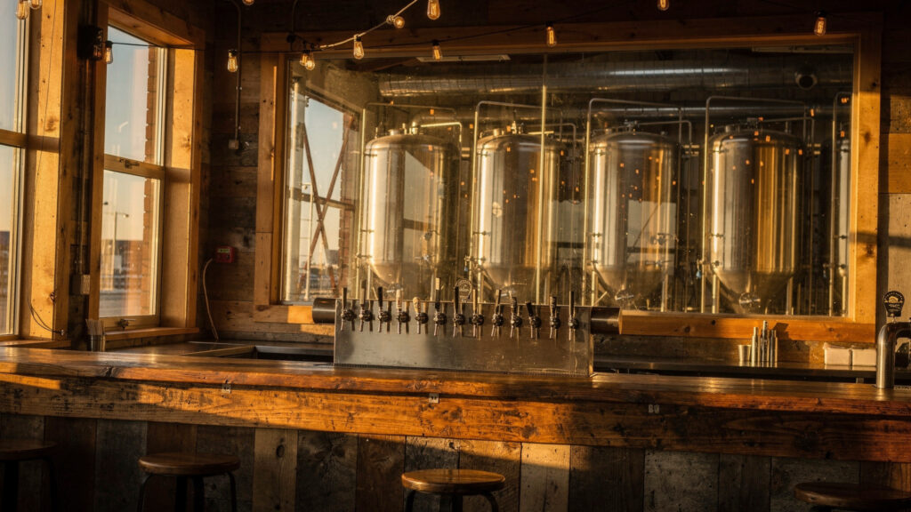 Taproom bar with beer taps and fermentation tanks visible through a window at an Abbotsford BC brewery