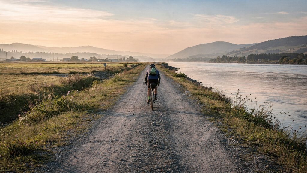 Cyclist riding along the flat gravel dyke trail beside the Fraser River at Matsqui Trail Regional Park