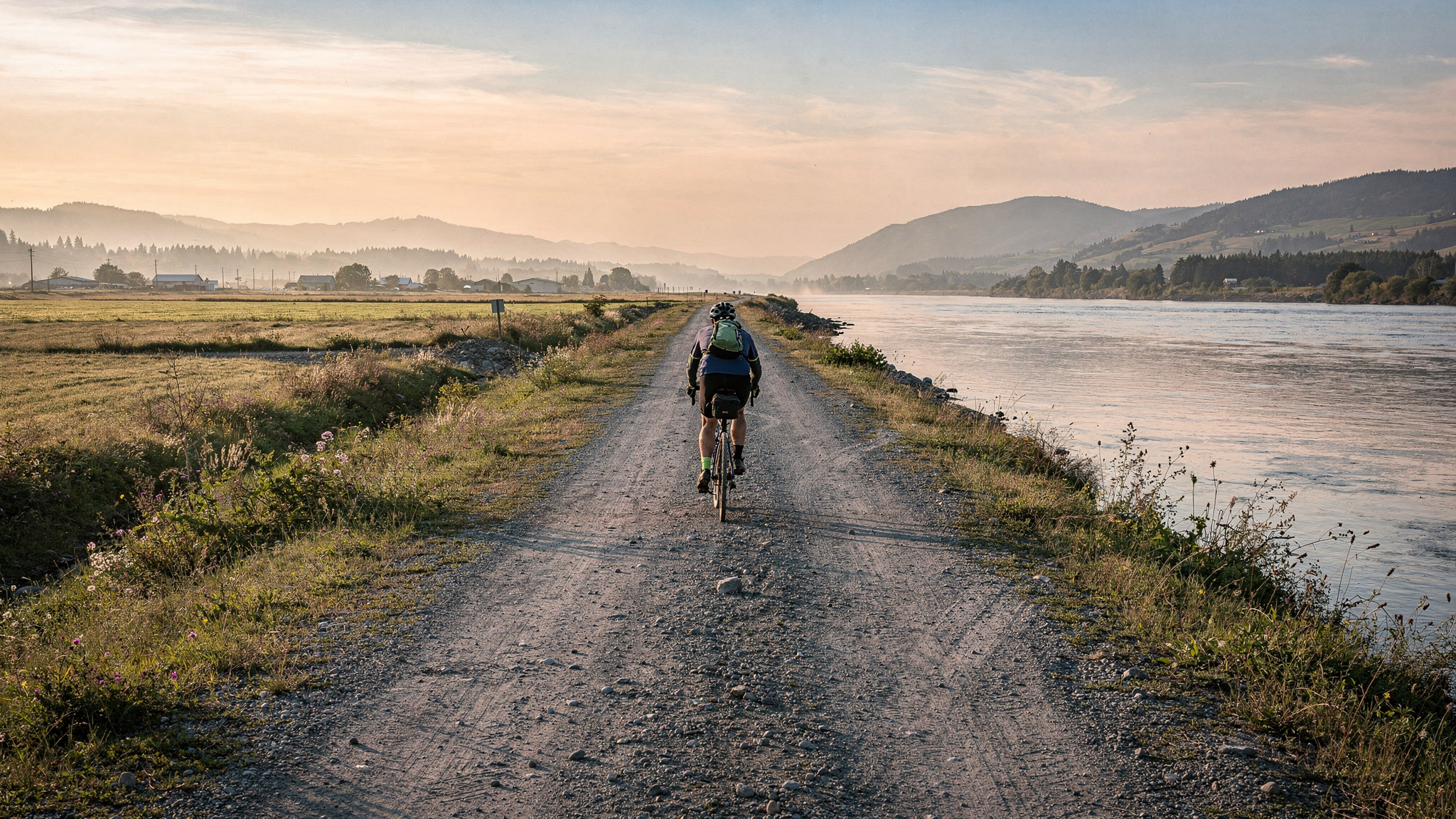 Cyclist riding along the flat gravel dyke trail beside the Fraser River at Matsqui Trail Regional Park