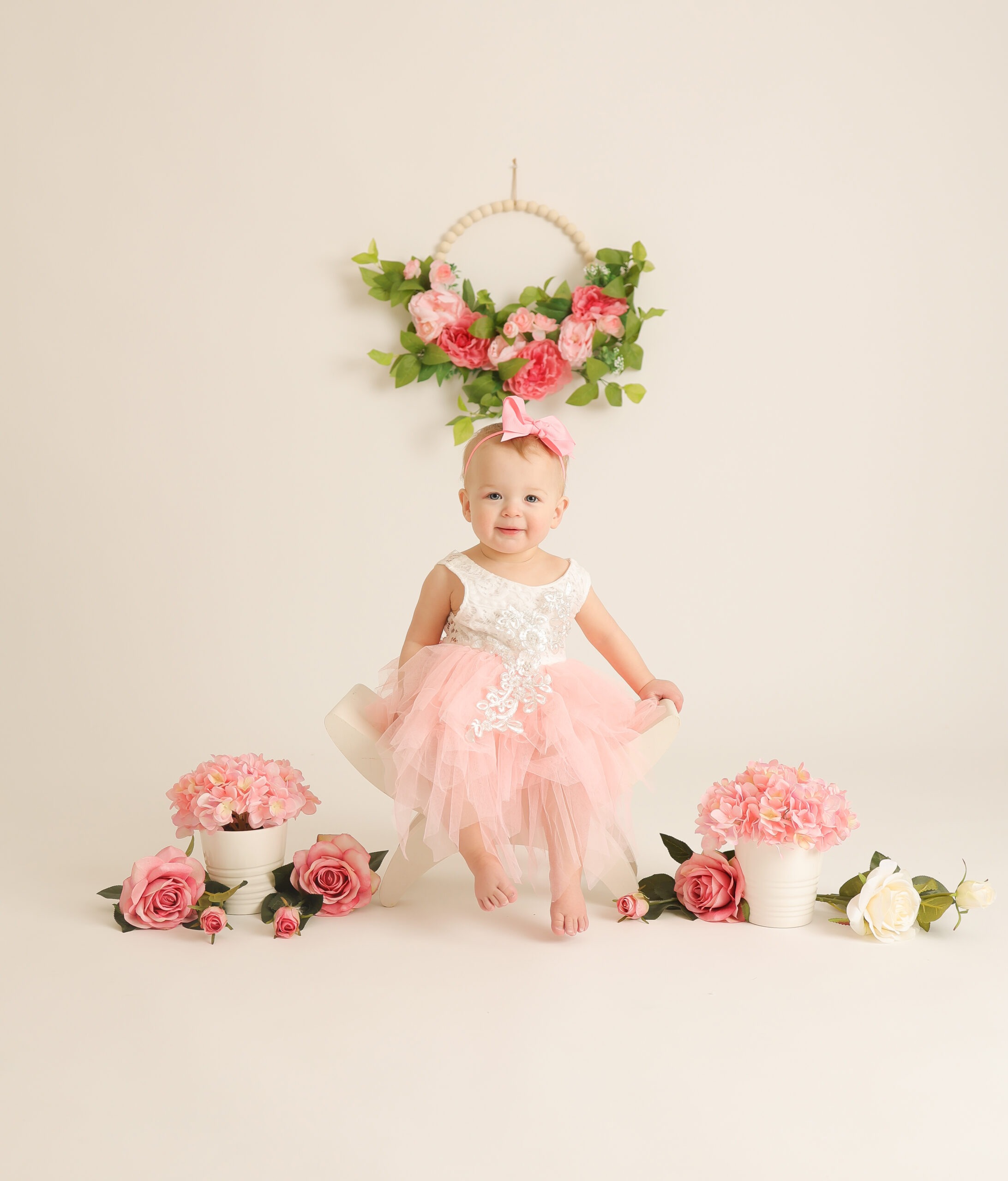 Baby sitting beneath floral arch with soft pink decor Natalia Vaxman Photography